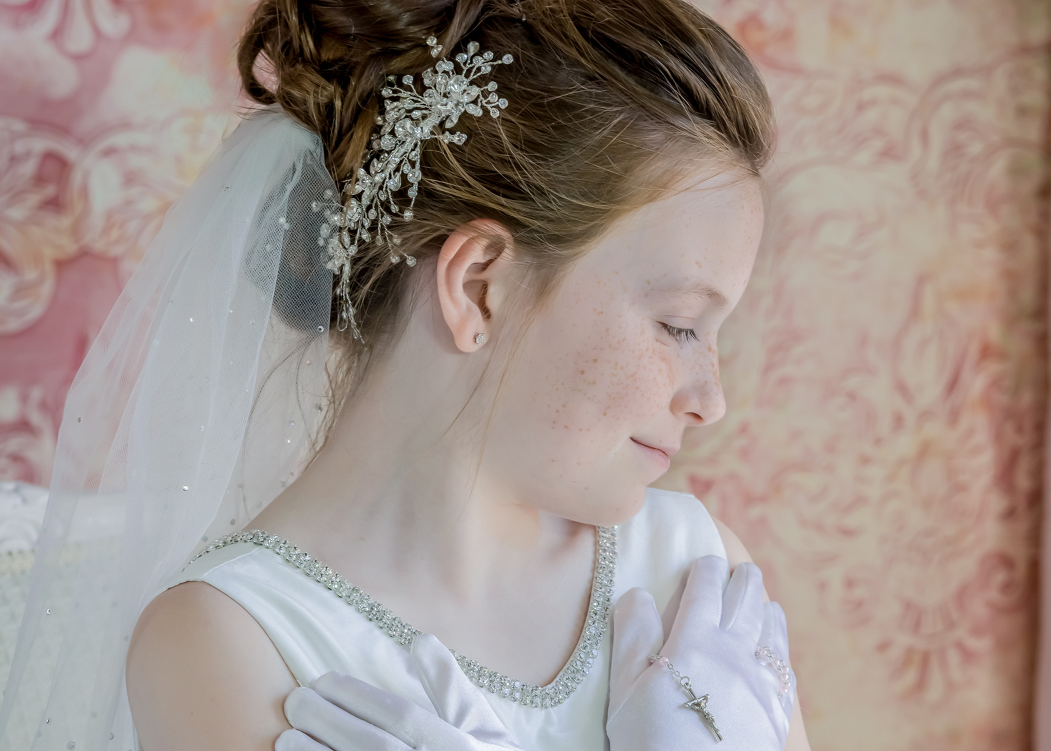A picture of a child in her Communion attire while holding a rosary.