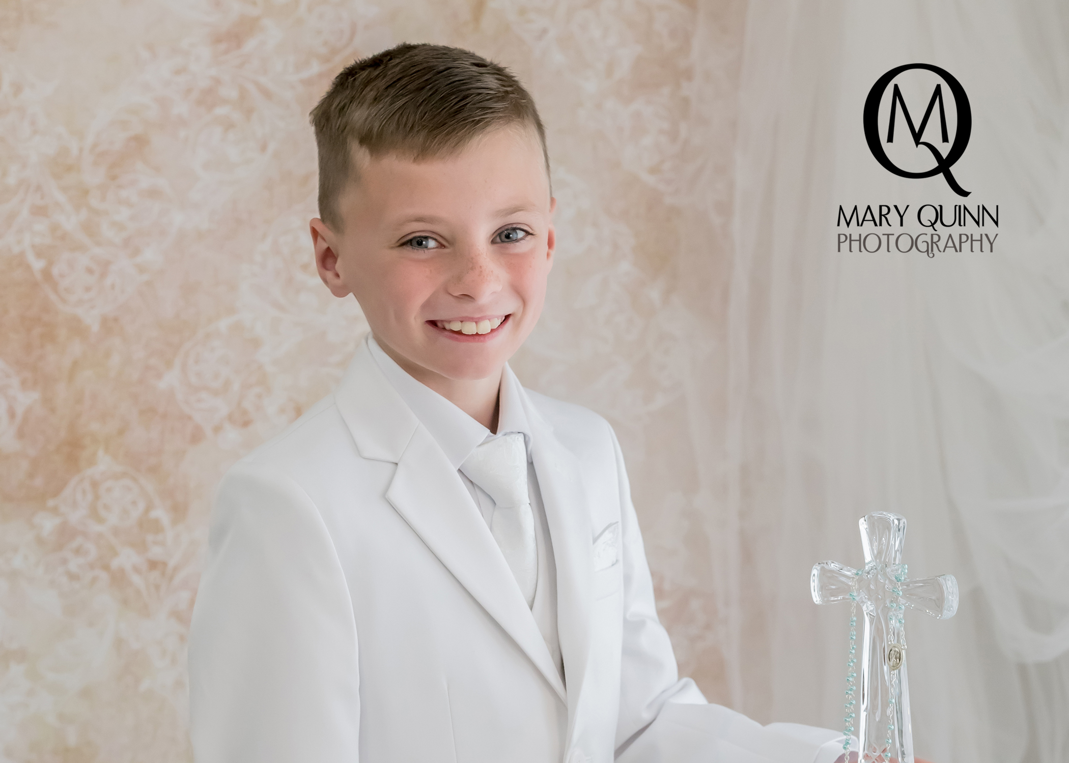 First Communion boy smiling and holding a cross in Evesham, New Jersey studio by Mary Quinn.